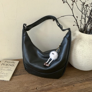 Detail of black faux leather hobo bag with a cute white plush monster charm on a desk