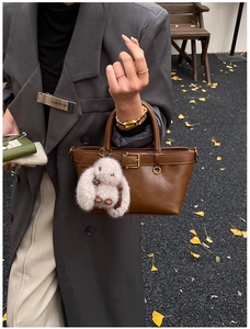 Detail of a brown leather tote with a plush rabbit charm and elegant buckle hardware