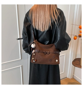 Detail of brown suede shoulder bag featuring star patches, bow, and a soft pom-pom charm