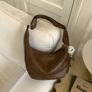 Brown faux leather crescent bag with adjustable strap and cute plush charm on a sofa