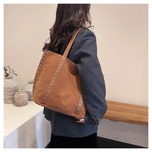 Brown suede tote bag with silver studs worn by a model in a warm indoor setting