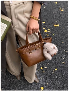 Brown vintage leather bucket bag with gold buckle and plush rabbit charm on autumn street