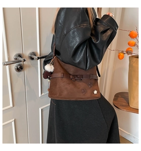 Detail of dark brown suede tote bag with leather bow decoration and white fur pompom accessory