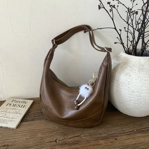 Detail of a brown vintage hobo bag with a plush doll charm on a rustic wooden table