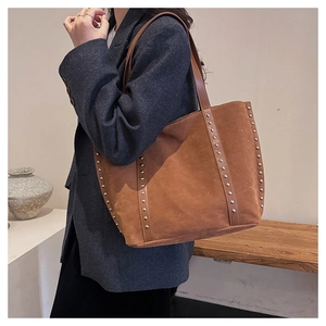 Macro detail of brown suede tote bag with silver studs on a minimalist indoor bench