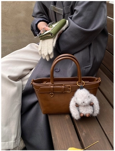 Detail of vintage brown leather handbag featuring a cute plush bunny charm and top handles