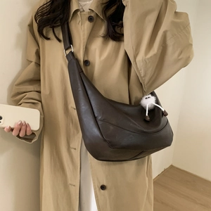 Detail of a dark brown crescent bag with soft pleats and a white plush charm