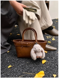 Detail of dark brown leather bucket bag with plush rabbit charm on autumn leaves background