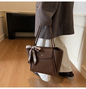 Close-up of brown lychee leather tote bag with silk scarf on handle and metal buckle