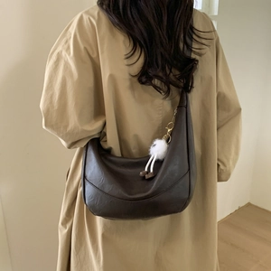 Detail of dark brown hobo shoulder bag with white plush charm on khaki trench coat