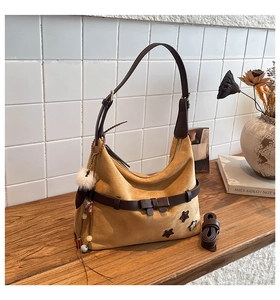 Detail of suede hobo bag with leather trim, bow accent and star patch on wooden table