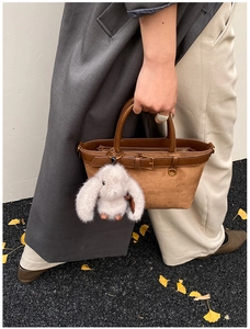 Close-up of brown suede tote bag with plush bunny charm in a street style setting