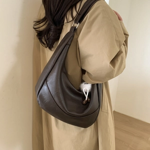 Detail of dark brown crescent shoulder bag with a plush charm and curved stitching
