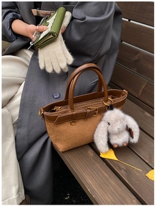 Close-up of brown suede bucket bag with leather handle and cute plush bunny charm