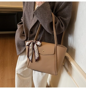Detail of khaki pebbled leather tote bag with silk scarf on handle and front flap pocket