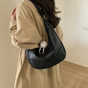 Detail of a black hobo shoulder bag featuring a white plush doll charm and soft leather