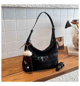 Detail view of black tote bag with star patch and plush glove charm on wooden table