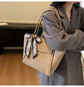 Detail of beige lychee leather tote bag with silk scarf on handle worn by a model