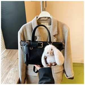 Detail of black leather handbag featuring gold buckle and a white plush rabbit charm