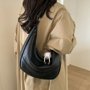 Detail of a black crescent hobo bag with plush charm on a model in a trench coat