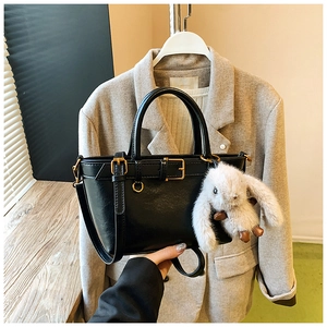 Close-up of black PU leather bucket bag with golden hardware and white bunny plush charm