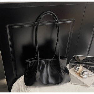 Detail of a black glossy pleated tote bag with slim handles in a modern office setting
