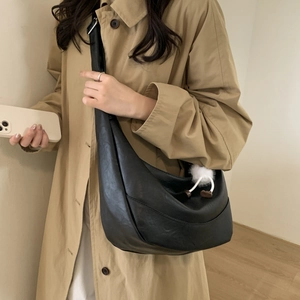 Side view of black matte leather crescent crossbody bag with white pompom charm