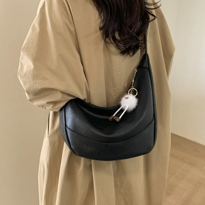 Close-up of black hobo shoulder bag with a playful white plush pendant on a model