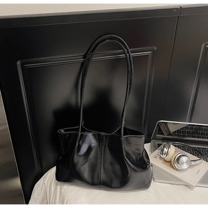 Detailed view of black pleated tote bag with glossy leather texture and laptop items