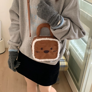 Détail du sac bandoulière en peluche caramel avec sourire porté avec une tenue d'hiver