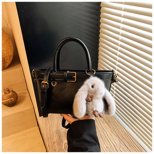Detail of black leather bucket bag with gold hardware and a cute plush rabbit charm