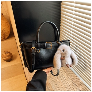 Detail of vintage black handbag with metal buckles and a gray plush rabbit charm