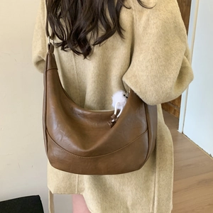 Detail of dark brown crescent bag with soft fur ball charm on PU leather strap