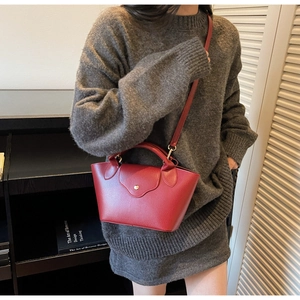 Detail of burgundy bucket bag with lychee texture and gold clasp on a gray sweater