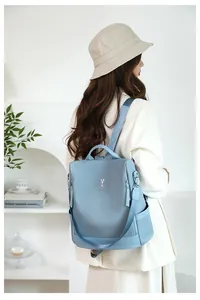 Rear view of a light blue soft leather travel backpack worn by a model in a minimalist room