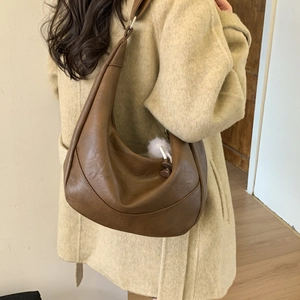 Detail of a brown half-moon shoulder bag with a soft faux leather texture and fur pendant