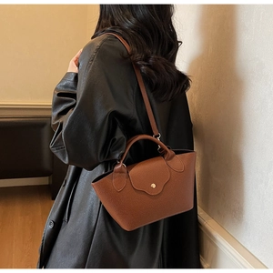 Detail view of brown lychee-patterned bucket bag with gold snap button on black leather coat