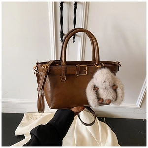 Detail of brown leather bucket bag with belt buckle and white plush rabbit charm