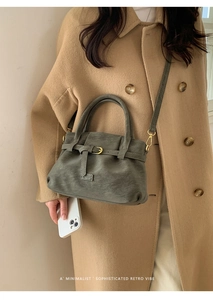 Close-up of sage green leather tote with metal buckle detailing on a wool coat