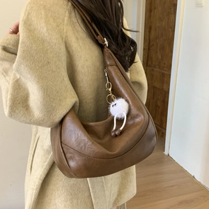 Brown leather-like Hobo shoulder bag worn with an oversized coat and a cute plush charm
