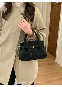 Detail of a black suede handbag with gold buckle and belt accent on a trench coat model