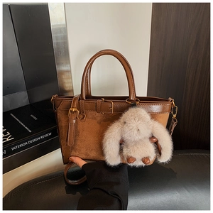 Detail of brown leather bucket bag featuring a decorative buckle and plush rabbit charm