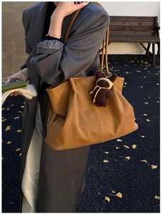 Detail of large brown matte tote bag with teddy bear charm in an autumn park setting