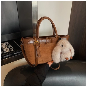 Detail of vintage brown tote bag with suede texture, gold buckle and plush rabbit charm