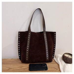 Detail of dark brown suede tote bag with silver metal studs on wooden table