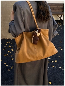 Side view of a camel matte tote bag with knit bear charm in an autumn outdoor setting
