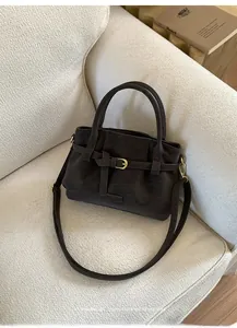 Detail of dark brown suede tote bag with golden buckle on a creamy white sofa