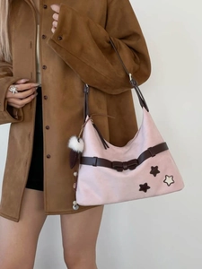Pink suede underarm bag with brown leather strap and plush ball charm on a model