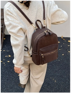 Détail d'un sac à dos en cuir marron avec surpiqûres blanches et fermetures éclair dorées