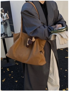 Close-up of caramel brown leather tote bag with woven charm on a model in grey suit